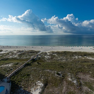 Expansive view of the tranquil beach with white sand, inviting turquoise waters, and a wooden walkway leading to the shore