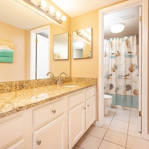 The master bath features a spacious granite countertop, colorful beach-themed decor, and a shower with a charming curtain