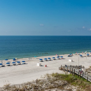The image showcases a serene beach front with colorful umbrellas and lounge chairs set against a backdrop of clear blue skies