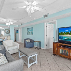 Living area with comfortable seating and a large TV showcasing a beautiful tropical beach scene