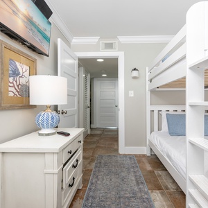 Cozy guest bedroom featuring a stylish queen bunk bed, decorative lamp, and a wall-mounted TV for entertainment