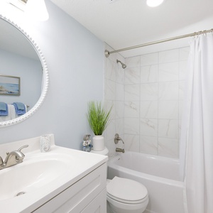 This bathroom features a stylish round mirror, light blue walls, and a clean design with white fixtures and soft towels