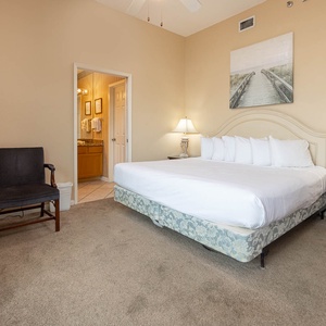 Bright and airy master bedroom features a king bed, cozy chair, and a view into the adjacent bathroom with elegant decor