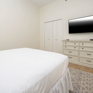 Queen bed, a flat-screen TV mounted on the wall, and a window with plantation shutters in this guest room