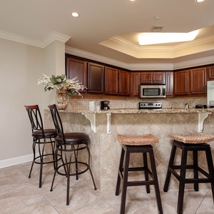 This kitchen features dark wood cabinetry, granite countertops, a stainless refrigerator, and a cozy bar area with seating