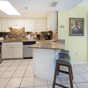 Bright kitchen with granite countertops, stainless appliances, and a breakfast bar with seating, leading to the master suite