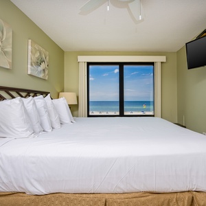 This bedroom features a plush king bed, soft white linens, and a stunning beachfront view through large windows