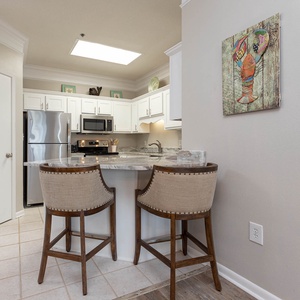 Bright kitchen area featuring white cabinetry, granite countertops, and a breakfast bar with two stylish stools