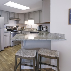A well-equipped kitchen features stainless appliances, granite countertops, and a cozy bar area with two upholstered stools