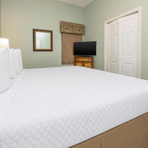 Inviting bedroom features a plush king bed with crisp white linens, a mounted TV, and soft green walls for a serene retreat