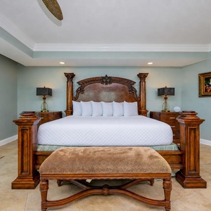 Master bedroom featuring a grand king wooden bed, elegant nightstands, and a plush bench in a serene setting