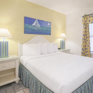 Cozy guest bedroom featuring a queen bed, cheerful yellow walls, and nautical decor with a vibrant painting above the bed