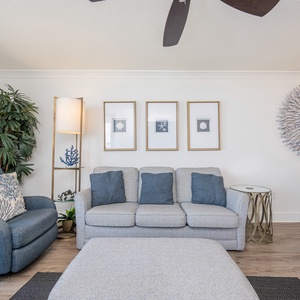 Cozy living area features a gray sofa with blue accents, a stylish accent chair, and beach artwork on the walls