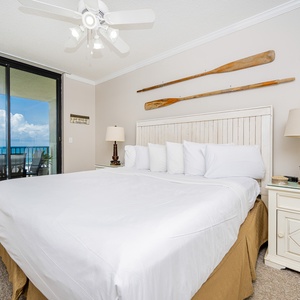 Master bedroom features a king bed with plush white linens, a dresser, and a balcony with gulf views