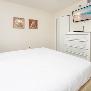 Soothing guest bedroom featuring a comfortable queen bed, a dresser, and a wall-mounted TV for relaxation and entertainment