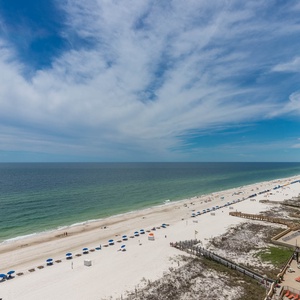 Enjoy breathtaking views of the beach, with white sand and colorful umbrellas lining the shoreline under a clear sky