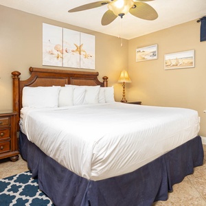 A cozy bedroom features a king bed with white linens, decorative artwork, and warm lighting from bedside lamps