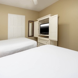 Rest in this comfortable guest bedroom featuring double beds, a TV, and a mirror, perfect for relaxation after a day of fun