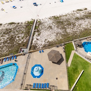 Overlooking the beach, this view showcases two inviting pools, lounge chairs, and a shaded gazebo area for relaxation