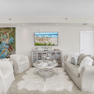 This living area features plush seating, a stylish coffee table, and a TV, all with a serene beach view