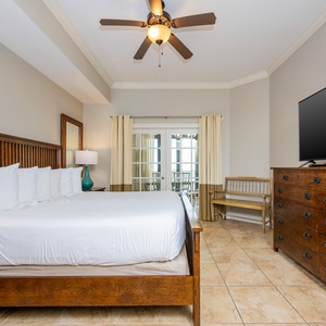 The master bedroom features a comfortable king bed, a large TV, and access to a private balcony with a lovely view
