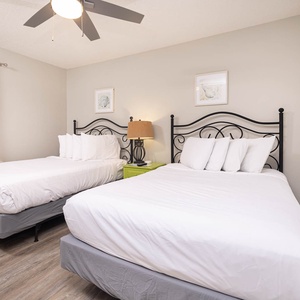 This guest room features two full beds with plush white bedding, a stylish lamp, and soft gray curtains framing the window