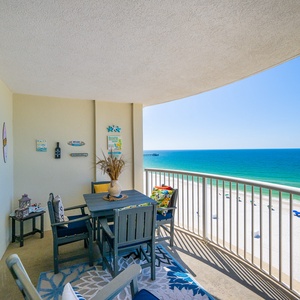 Enjoy a relaxing view from this balcony with wooden seating, colorful cushions, and a vibrant area rug overlooking the beach