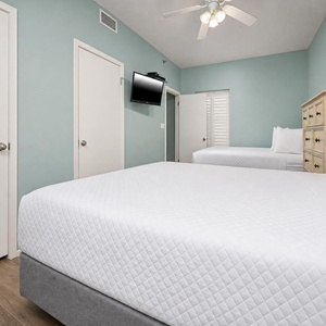 Brightly colored walls frame a cozy guest bedroom featuring two queen beds, a dresser, and a wall-mounted TV