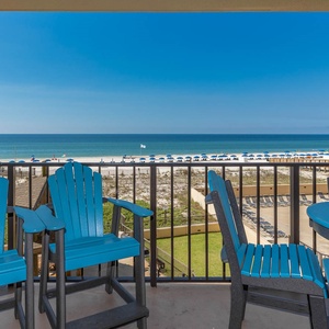 Bright blue Adirondack chairs and a table offer a perfect spot to enjoy the scenic beachfront view from the balcony