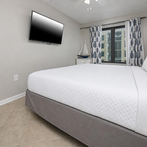 Cozy master suite with a comfortable bed, a mounted TV, and a lovely view through large windows with stylish curtains