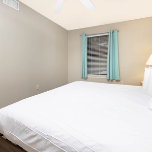 A cozy guest bedroom features a comfortable king bed with crisp white linens, soft teal curtains, and a warm bedside lamp