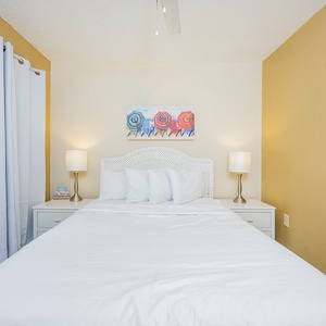 Guest bedroom featuring a queen bed, soft lighting, and cheerful beach-themed artwork for a relaxing getaway