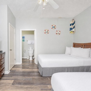 Brightly decorated guest room featuring two double beds, a TV, and nautical-themed wall art, with an adjoining bathroom
