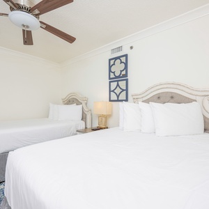 Guest bedroom featuring two queen beds with plush white bedding, a stylish lamp, and decorative wall art above the headboards