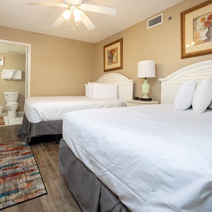 Guest bedroom featuring a queen and double bed, a colorful area rug, and a cozy ambiance with a ceiling fan and artwork