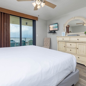 This inviting master bedroom features a plush king bed, elegant dresser, and a balcony view with seating for relaxing