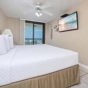 The master bedroom featuring a plush king bed, ceiling fan, and a TV, with sliding doors leading to a balcony view