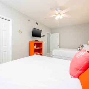 Guest bedroom featuring two queen beds, an orange accent shelf, and a wall-mounted TV for entertainment
