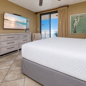 Cozy master bedroom with a large TV, stylish decor, and direct access to the beach balcony for fresh coastal air