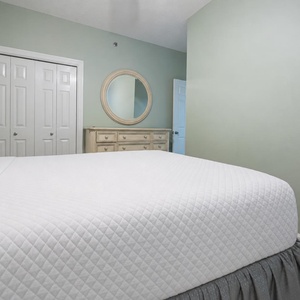 Inviting guest bedroom featuring a queen bed with crisp white linens, a stylish dresser, and a soothing green wall color