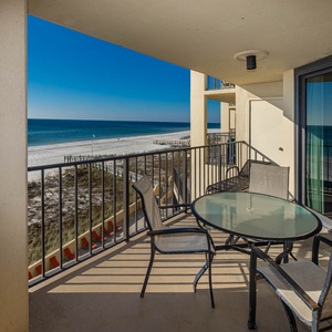 The balcony features a glass-top table and chairs, offering a serene view of the tranquil beach and azure waters