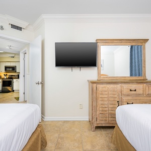 The bedroom has a wall-mounted TV and a glimpse of the modern kitchen, dining, and living space through the open door