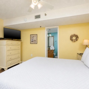 The bright yellow bedroom features a king bed, a TV mounted above a dresser, and an ensuite bathroom