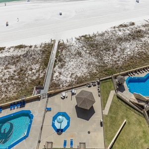 The view showcases the vibrant pool area with lounge chairs, a shaded gazebo, and easy access to the beach beyond