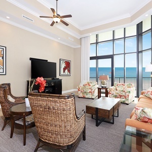 This living area features tropical-themed seating, a TV, and stunning beachfront views through large windows