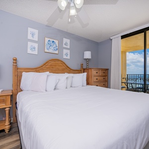 Brightly decorated master bedroom features a king bed, bedside lamps, and a balcony offering a beautiful beach view