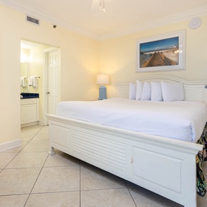 Master bedroom featuring a king bed, soft lighting, and a vibrant beach artwork, with an adjoining bathroom