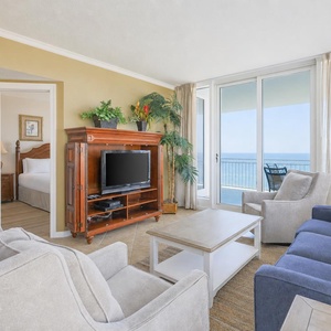 This living area features a cozy seating arrangement, a TV, and a stunning beachfront view through large glass doors