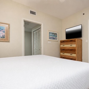 Guest bedroom featuring a comfortable king bed, a dresser, and a wall-mounted TV, complemented by beach-themed artwork