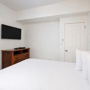 Cozy guest bedroom featuring a comfortable queen bed, a wooden dresser, and a flat-screen TV for relaxing evenings